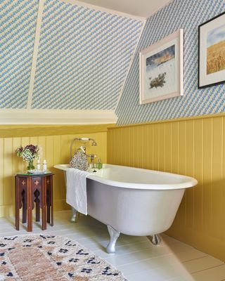 Attic bathroom with yellow paneling and ditsy blue wallpaper with freestanding bath