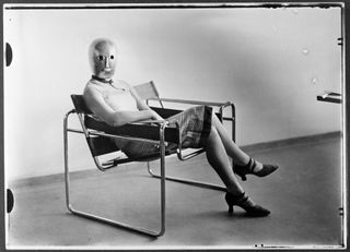 Woman wearing an Oskar Schlemmer mask sitting on Marcel Breuer’s Wassily Chair