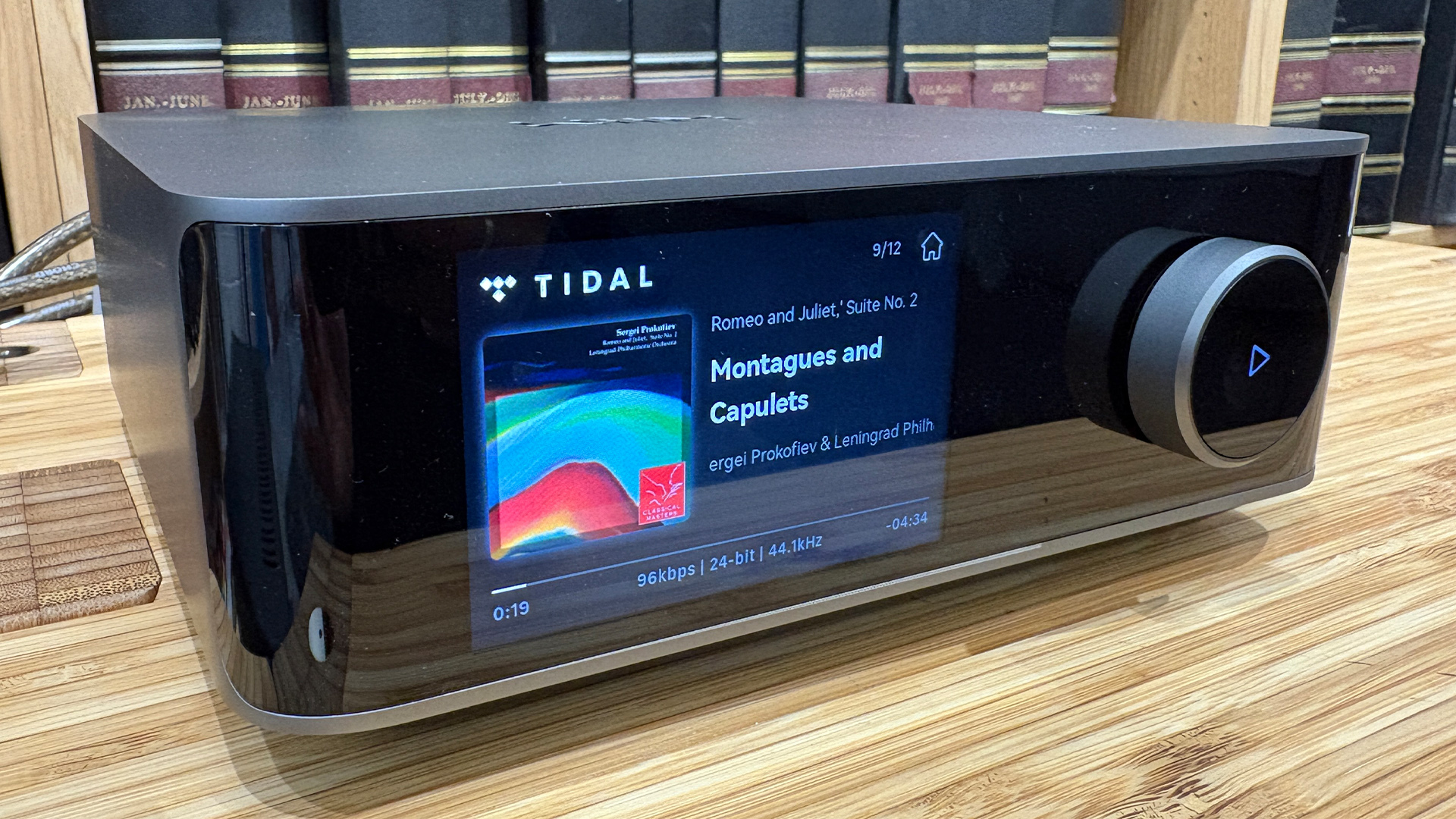 WiiM Amp Ultra streaming amplifier on wooden hi-fi rack in front of bookcase