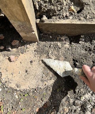 A person holding and using a trowel to smooth concrete surface for fencing