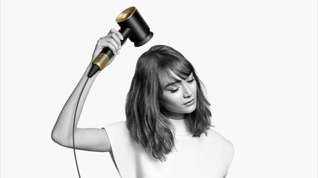 black and white image of woman with short hair drying hair with dyson limited edition onyx and gold supersonic dryer 