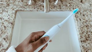 How to use an electric toothbrush: Image shows hand holding a toothbrush