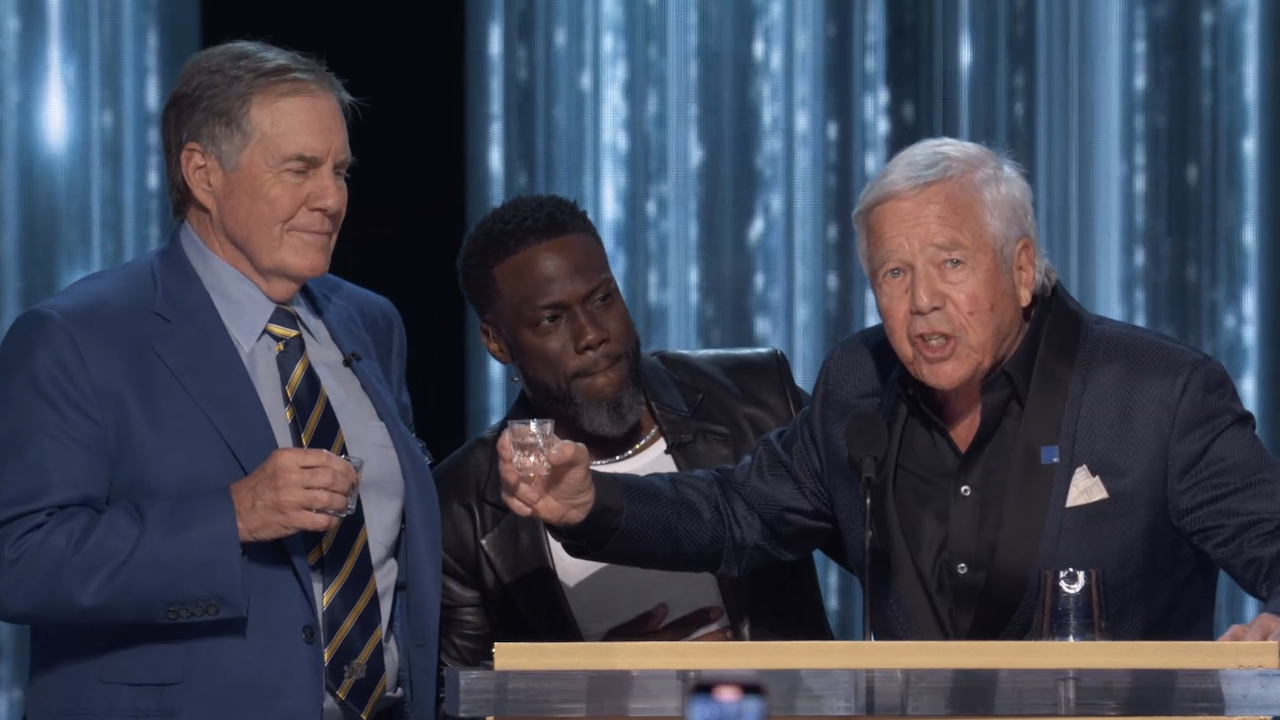 Bill Belichick and Robert Kraft toasting a shot in front of Kevin Hart on stage at The Roast of Tom Brady