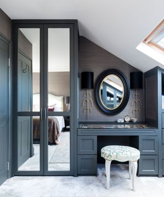 A bedroom with a gray wardrobe and dressing table with a stool