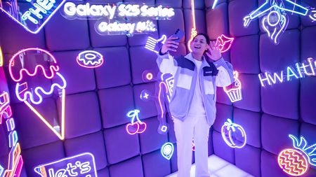 Promo photography for the Samsung Galaxy S25 Ultra showing a person holding the smartphone in a neon-lit booth.