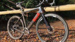 A muddy 3T Exploro gravel bike propped up against a wooden pole