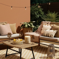 Very garden sofas on check rug in garden. There is a coffee table with two wine glasses, a candle and bowl of nachoes.