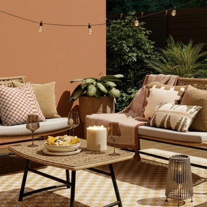 Very garden sofas on check rug in garden. There is a coffee table with two wine glasses, a candle and bowl of nachoes.