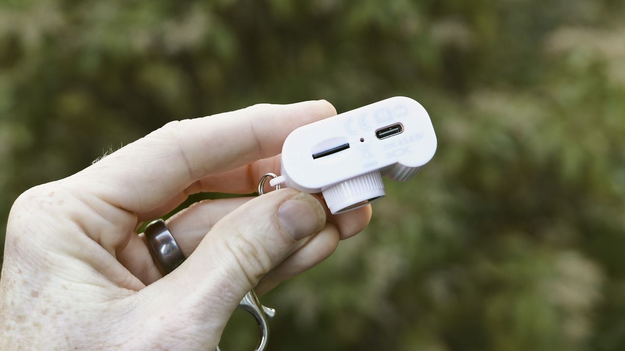 Miniature pink keychain camera, the 'Photo Creator Mini Digital Camera series 3', in user's hand, its underside