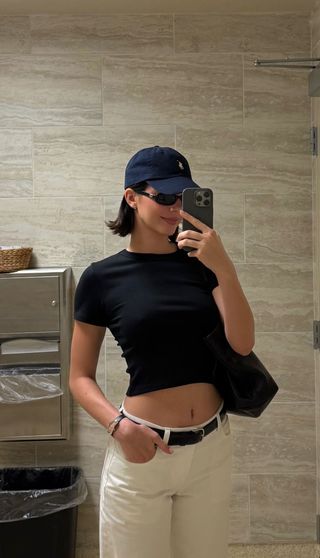 A photo of Kendall Jenner styling a navy baby tee with belted white jeans and a navy Polo Ralph Lauren baseball cap.