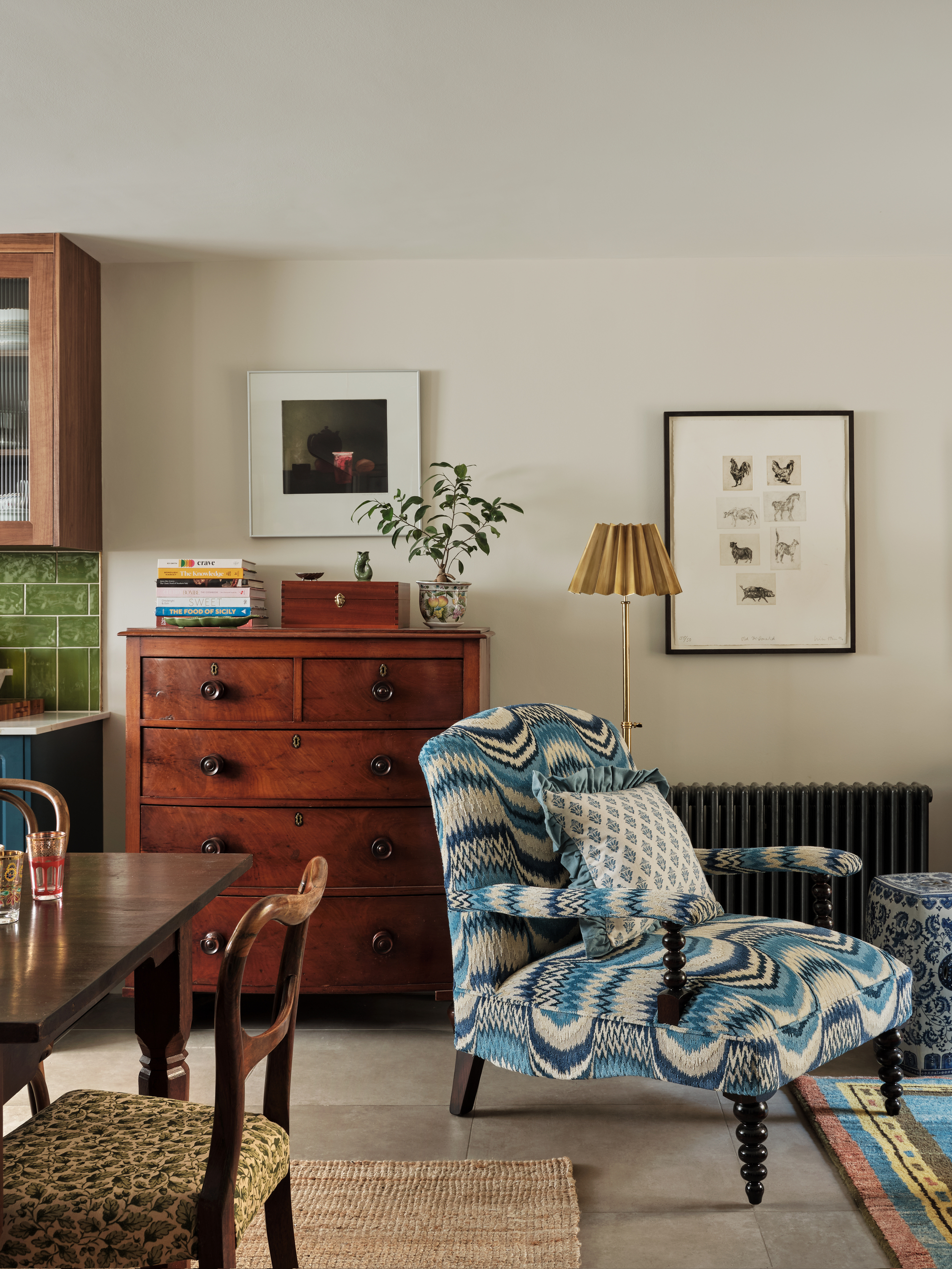 A living space with wooden chest of drawers, patterned dining chairs, and a blue, wavy patterned armchair