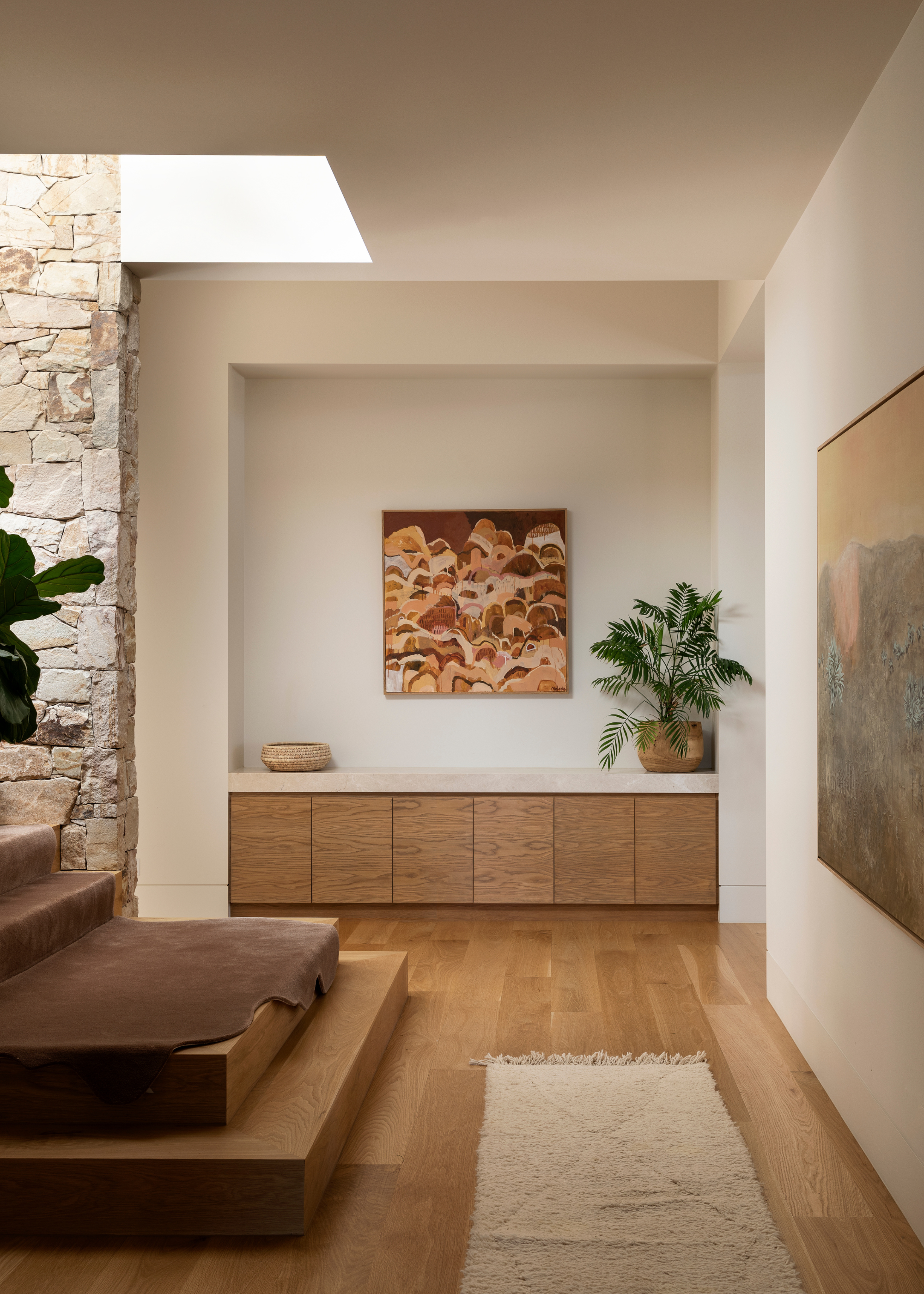 An entryway with a staircase, a textured runner, a storage nook with cabinets, a potted palm, and a hanging painting