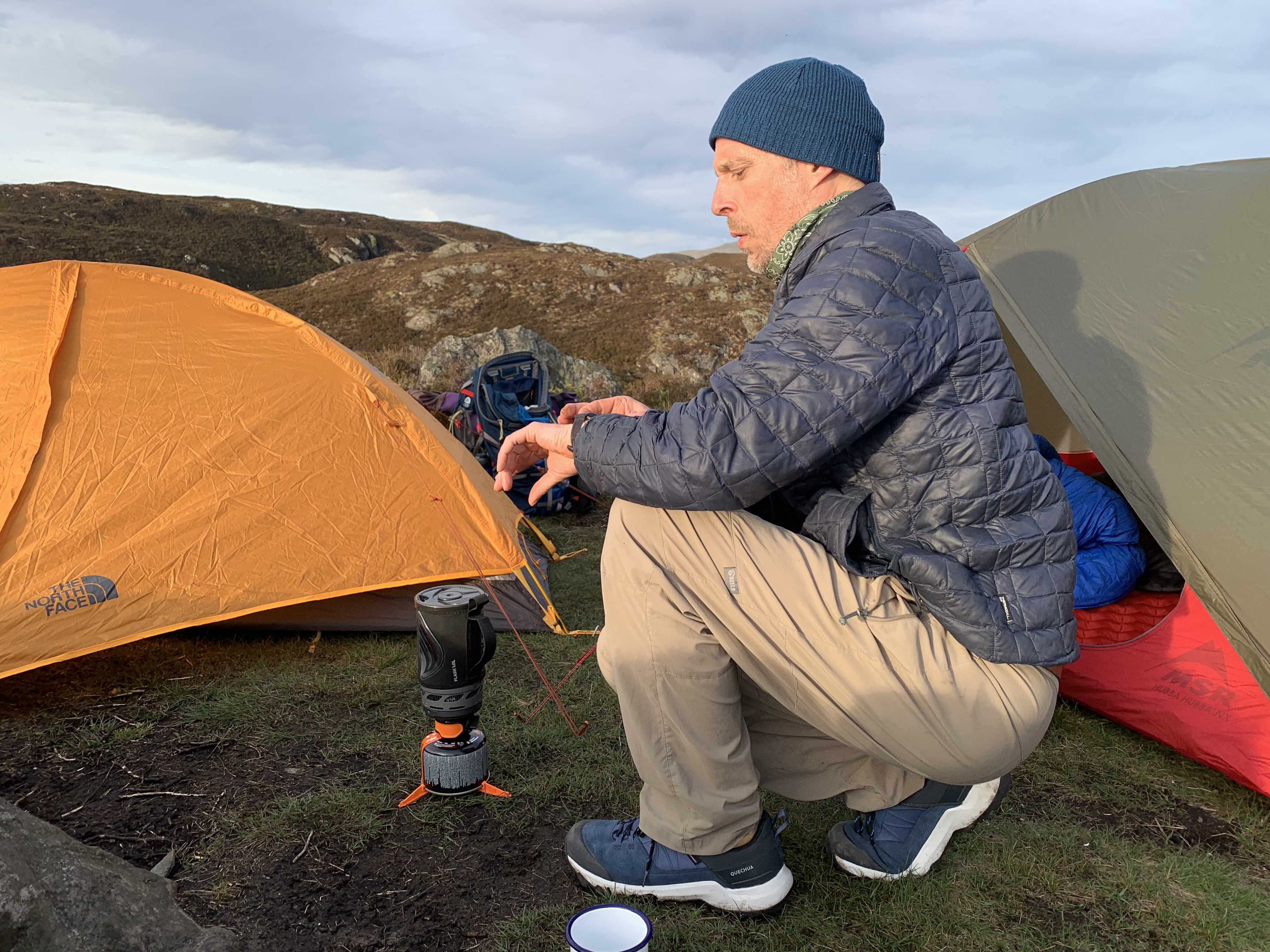 Man checking his watch while cooking with the Jetboil Flash 1.0 next to a yellow tent