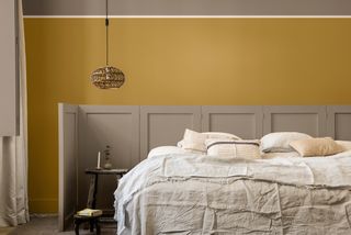Mustard wall painted in bedroom with natural taupe bedding