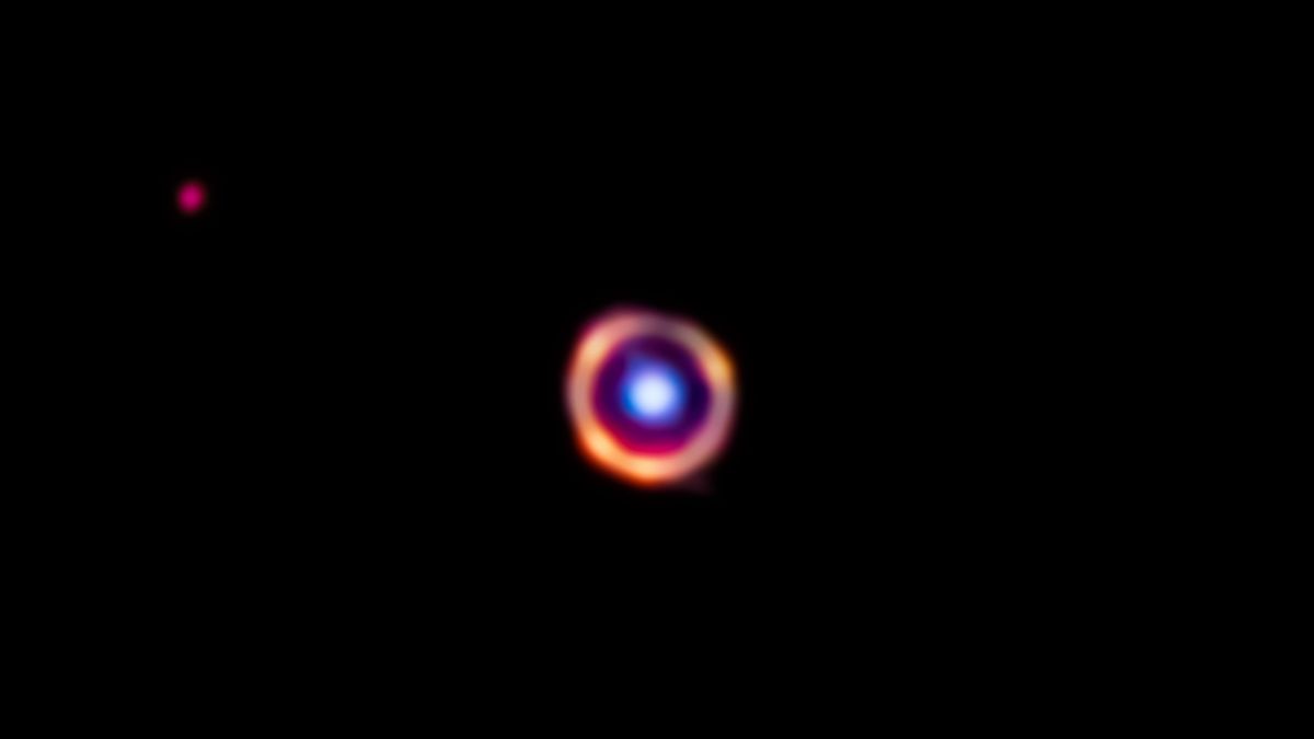 James Webb Space Telescope image of a complex organic molecules in a distant galaxy, shown as a blurry red ring around a light-blue splotch that is a foreground galaxy.