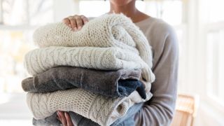 person holding a pile of clean jumpers