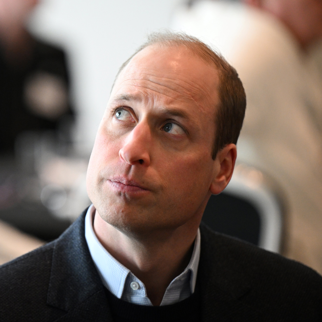 Prince William wears a shirt with a sweater and looks serious