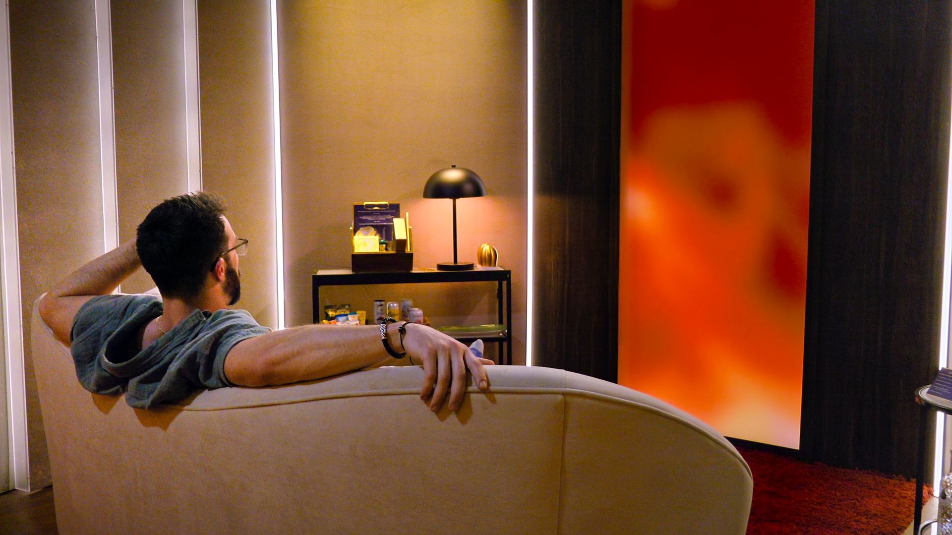 john sits on a couch in the pods while looking at an orange wall in love is blind season 11
