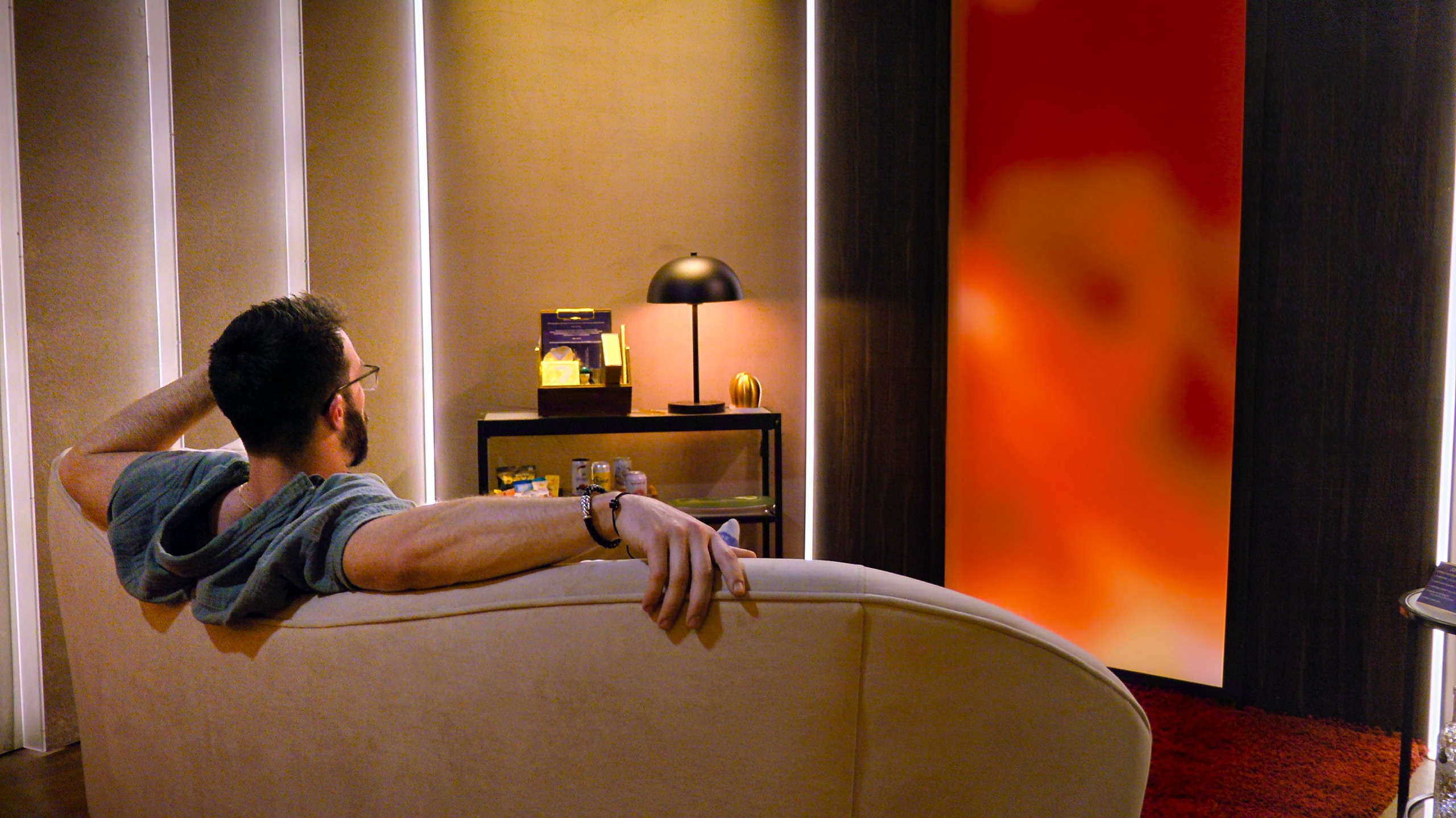 john sits on a couch in the pods while looking at an orange wall in love is blind season 11