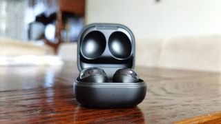 A pair of the Samsung Galaxy Buds Pro in grey in their charging case, resting on a table.