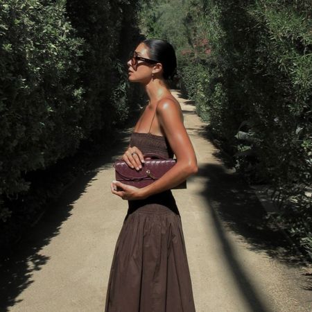 Woman wears brown shirred dress and carries burgundy Bottega Veneta bag
