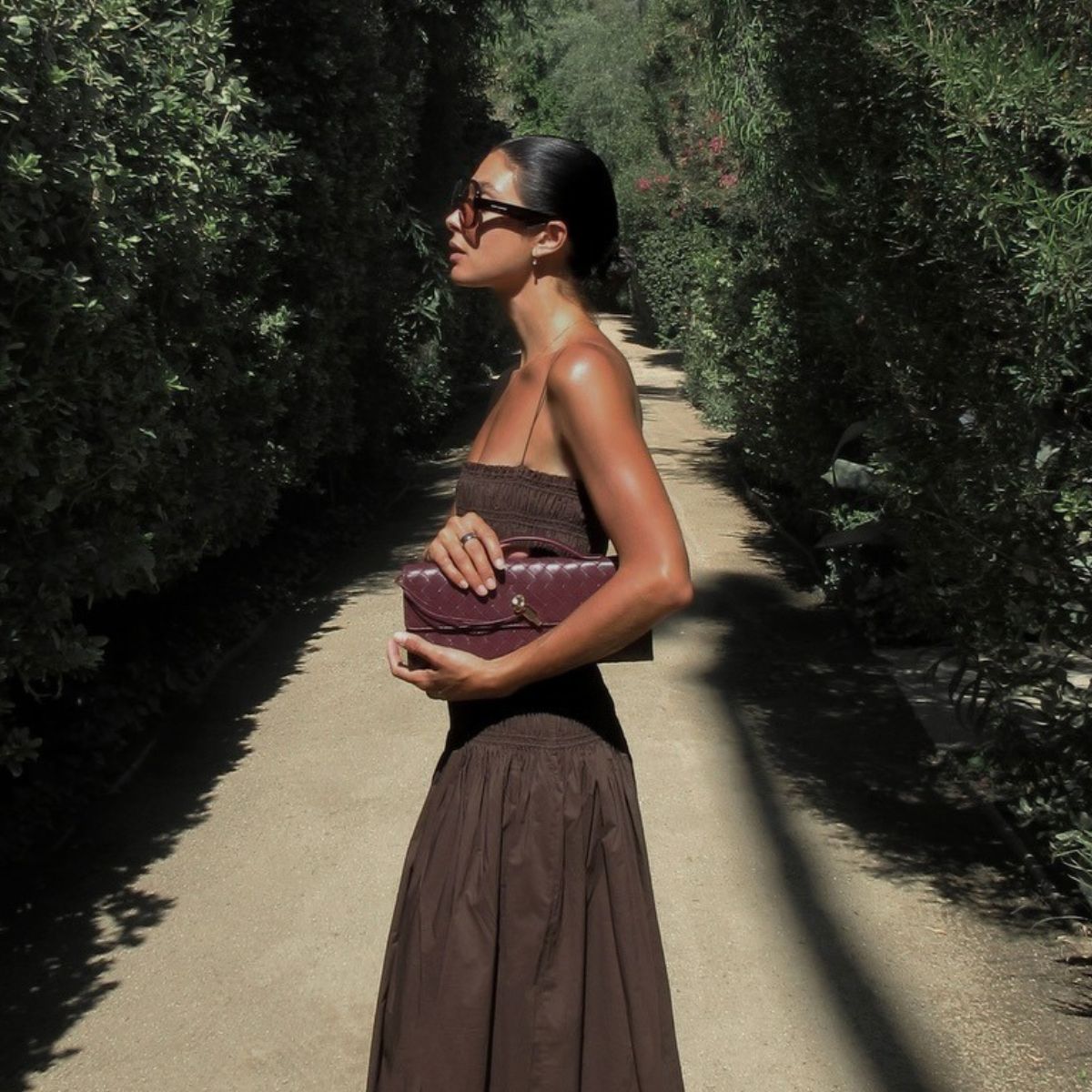 Woman wears brown shirred dress and carries burgundy Bottega Veneta bag
