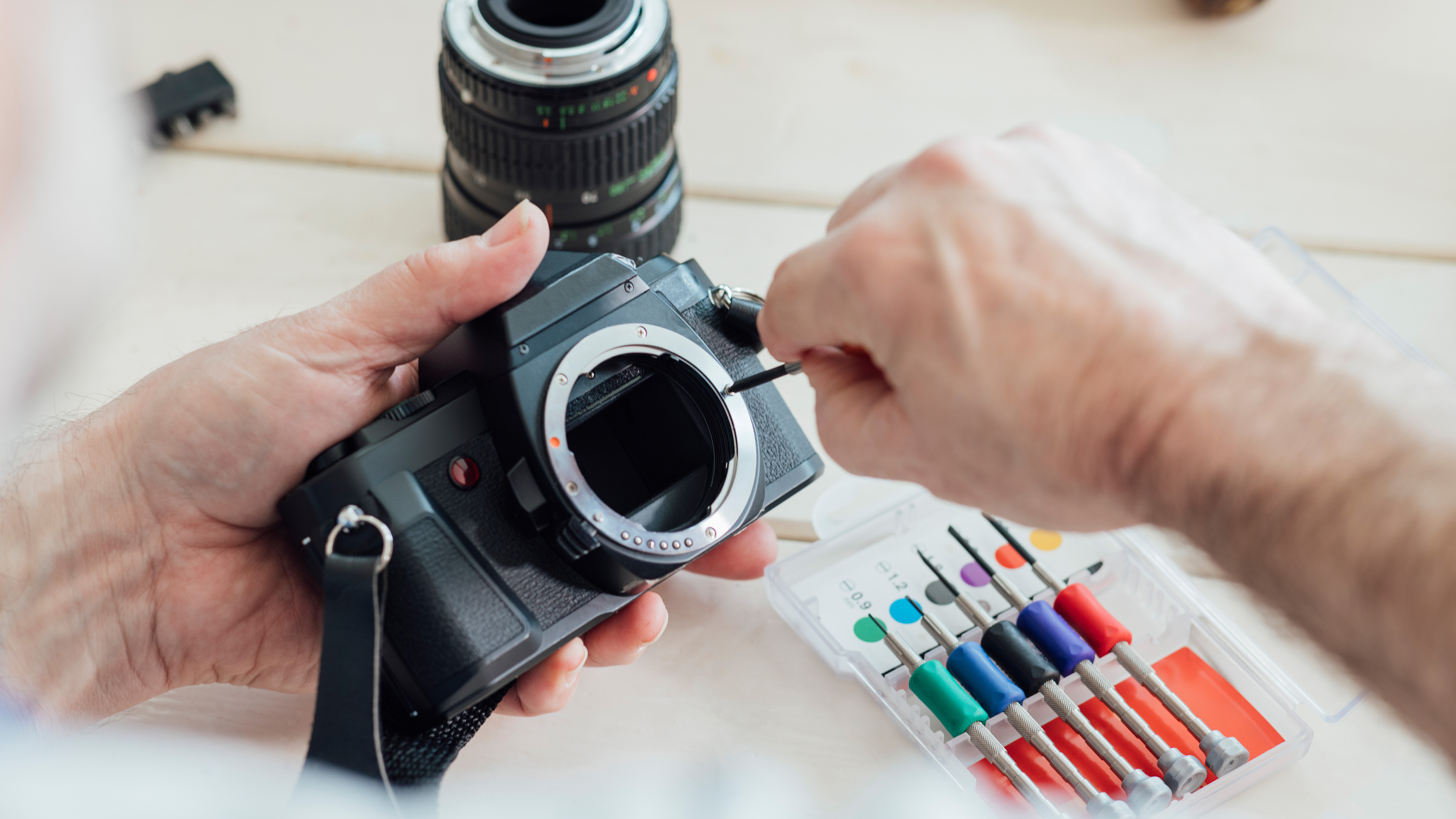 Man&#039;s hands repairing an SLR camera with a screwdriver