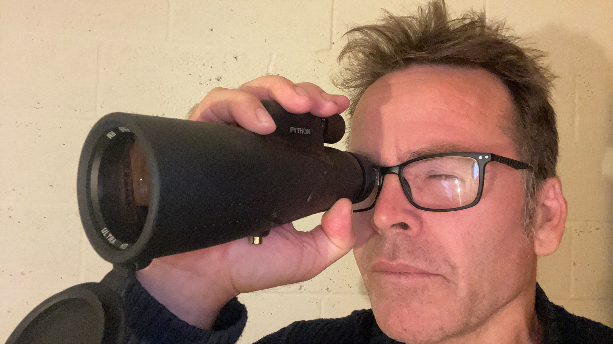 A man with glasses holding a monocular up to one eye.