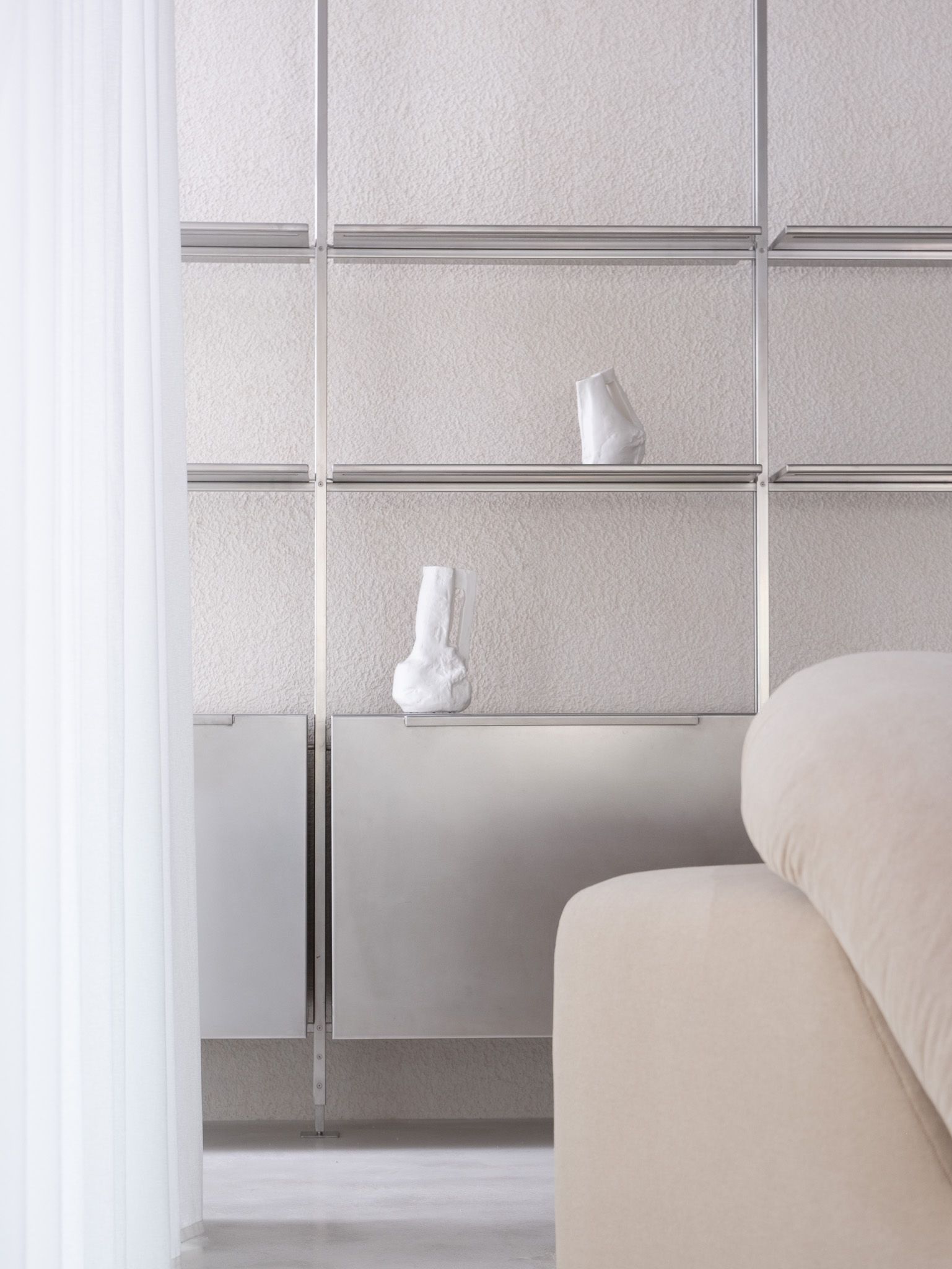 The interior of a brutalist, minial design showroom, decorated with contrasting furniture, artworks, and accessories in wood, earthy fabrics, reflective surfaces, and plants.
