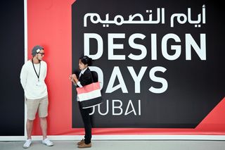A large red, black and white Design Days Dubai sign with two people standing in front of it