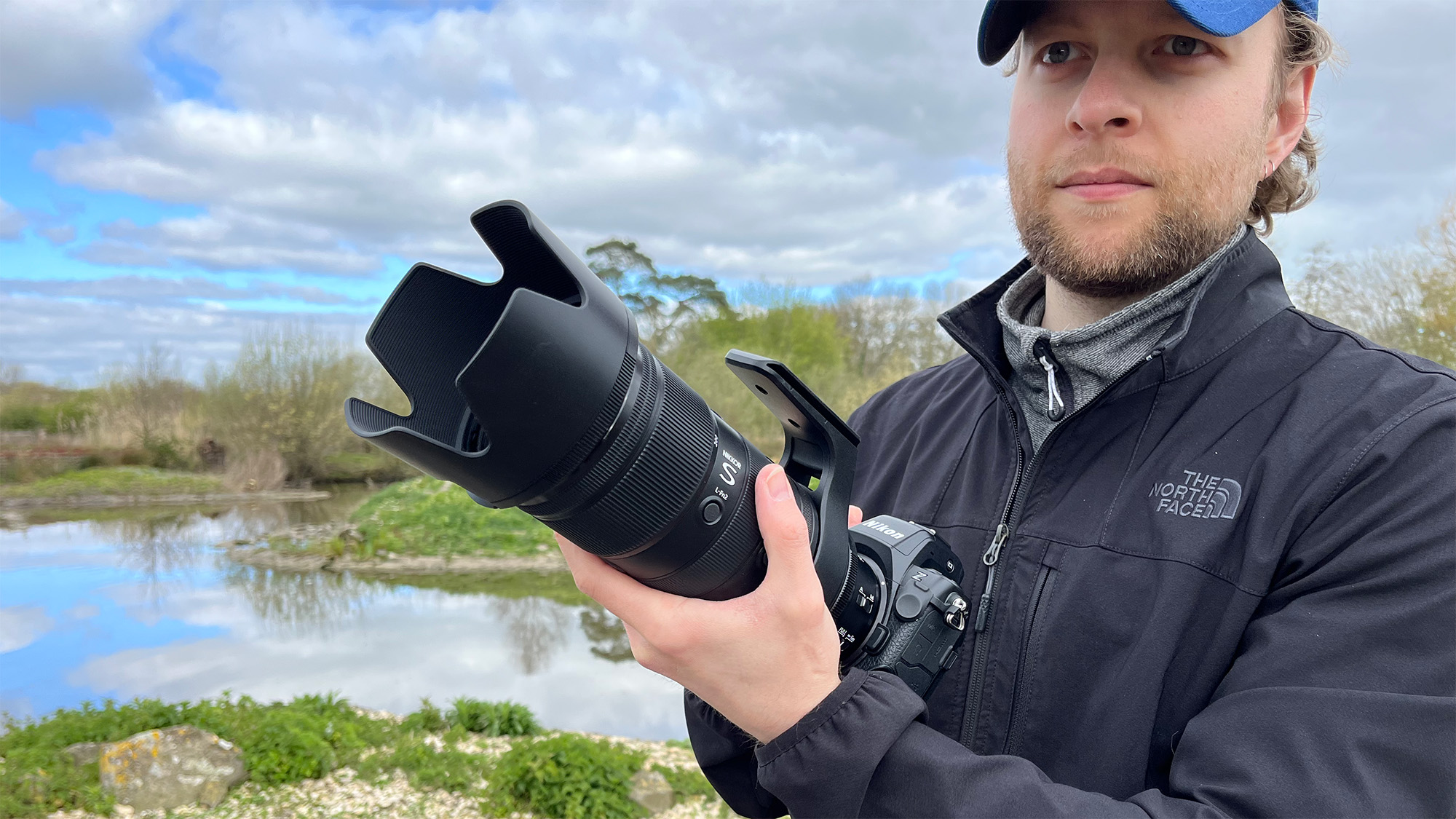 Mike Harris holding Nikon Z 70-200mm f/2.8 VR S II by a lake with vegetation and trees in the background