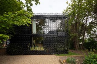 A house with a black metal lattice facade surrounded by woodland