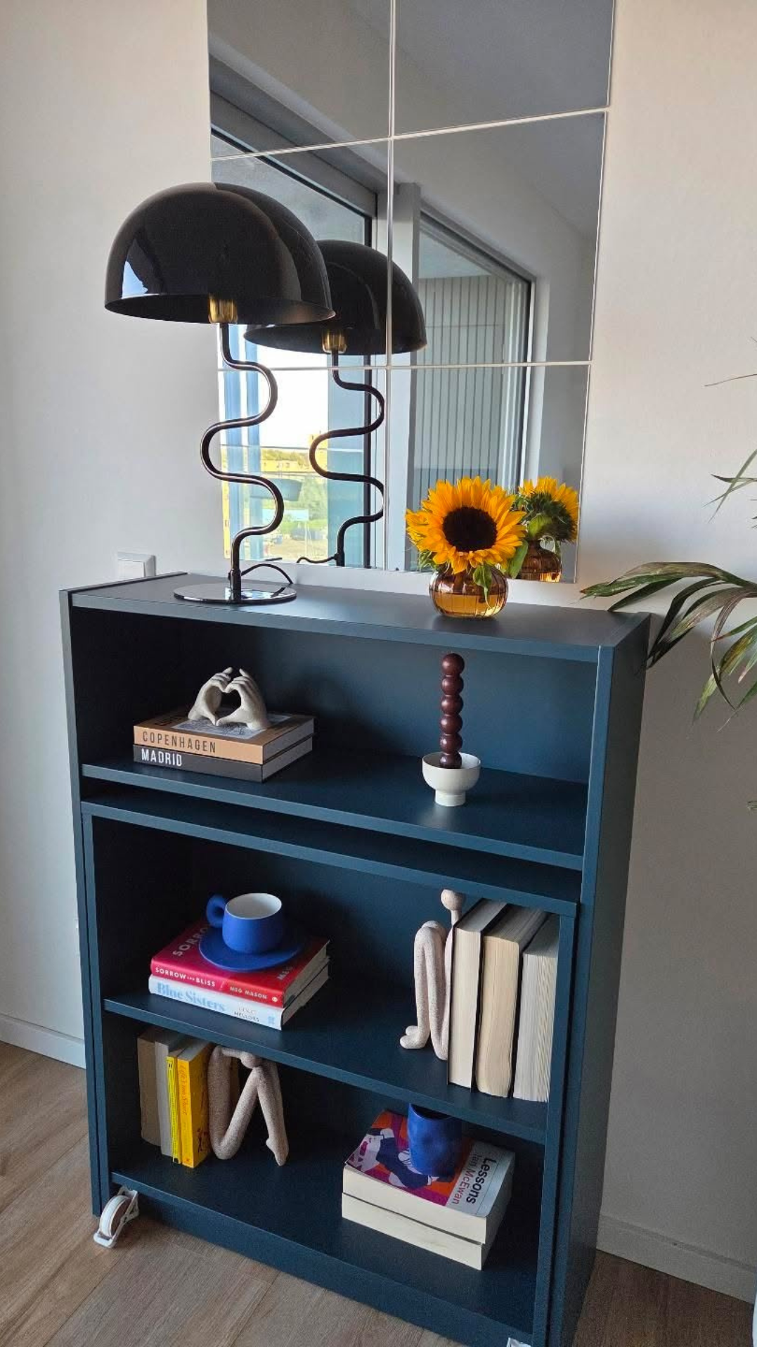 A blue-gray bookcase decorated with various trinkets and a sunflower.