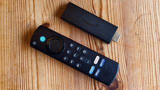 The Amazon Fire TV Stick on a wooden table beside its remote.