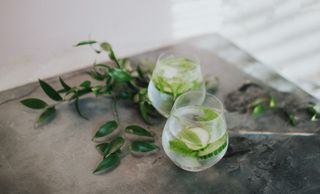 Cold refreshing glass of clear liquid Gin and tonic or water garnished with mint and cucumber on a stylish concrete surface Space for copy