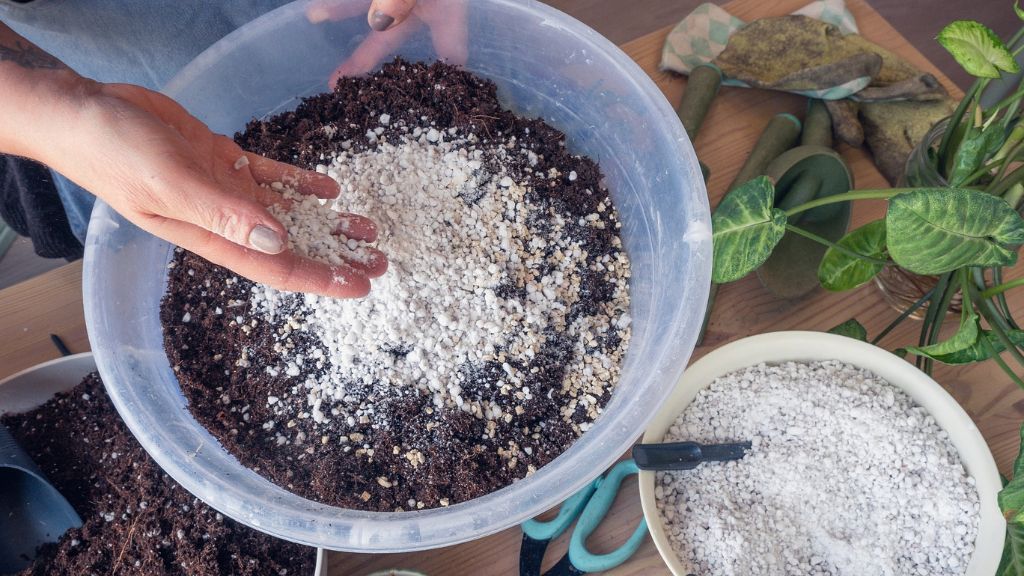 A hand dropping perlite into a pot of soil