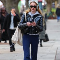 Sophie Turner in a leather jacket, blue pants, and a hoodie