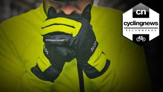 Cyclist in high vis cycling clothing and Gore Windstopper gloves blows into his hands to try to warm them up