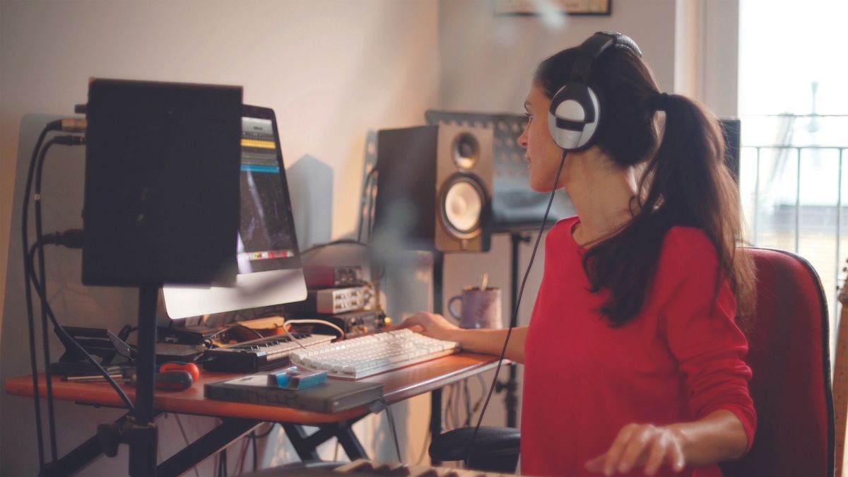 A woman sits at a desk making music on a computer