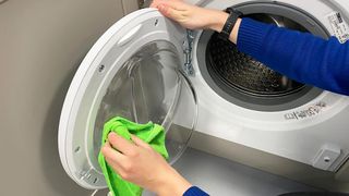 Person using a green microfiber cloth to clean the inside of a washing machine door.