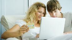 Blonde woman holding a credit card looking at a laptop with her teenage son
