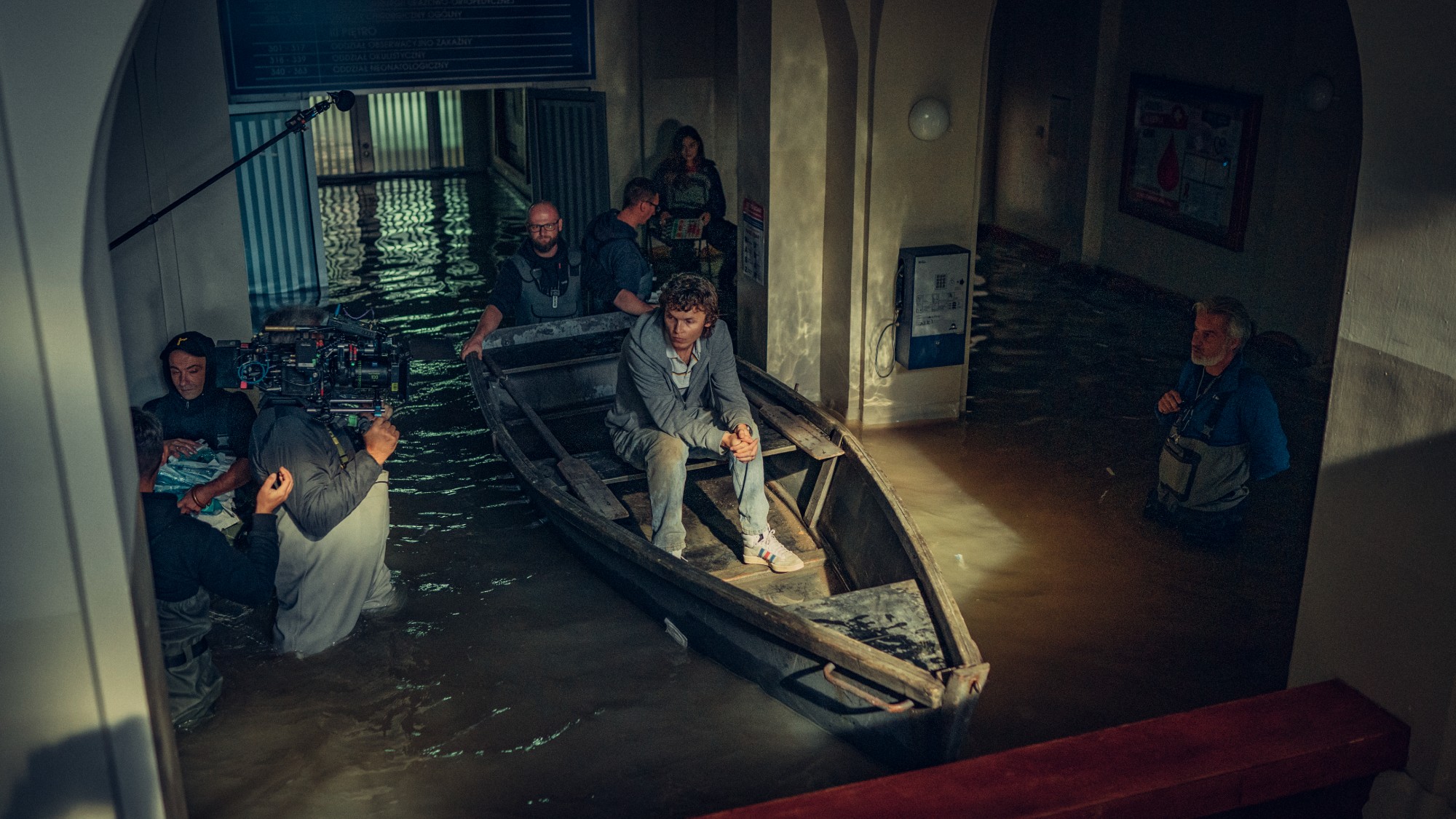 3/4 shot of a bunch of people in and around a small wooden boat inside a building as flood waters rise