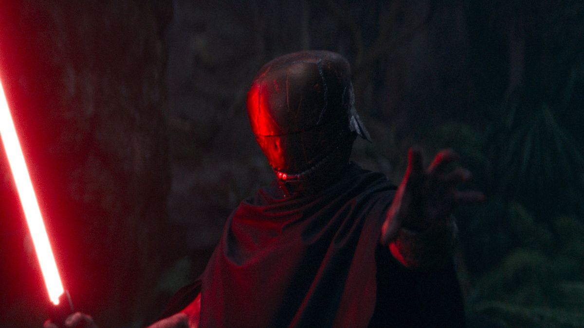 Manny Jacinto&#039;s Acolyte character Qimir masked and holding red lightsaber