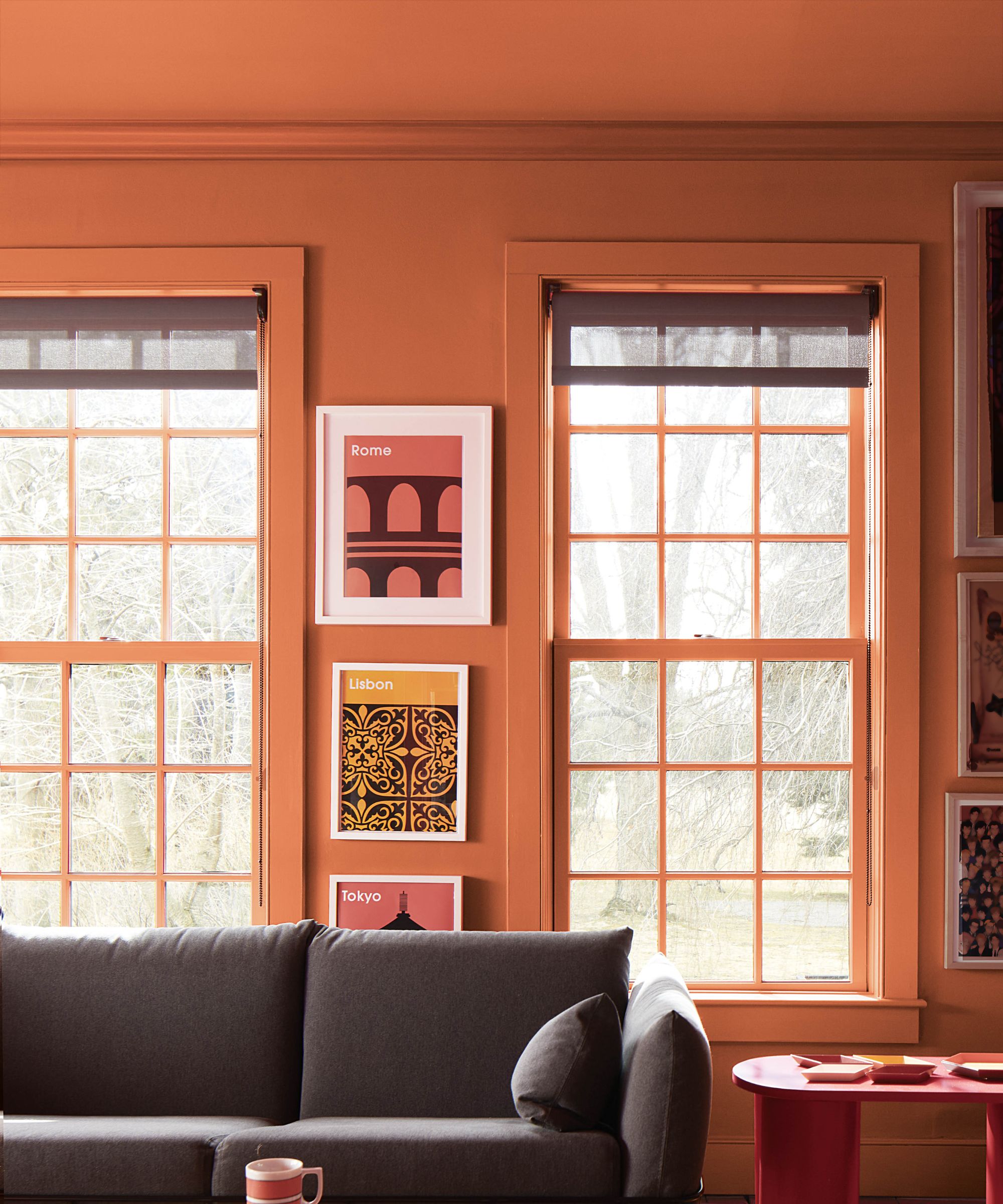 Warm-toned sitting room with terracotta walls and matching window frames, creating a playful, colour-drenched space with curated gallery art.