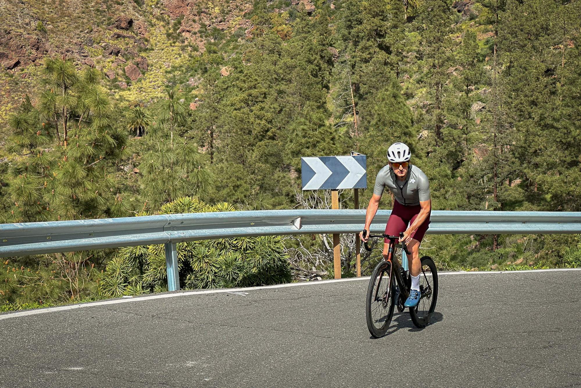 Man wearing green jersey, red shorts and white helmet riding out of the saddle towards the camera