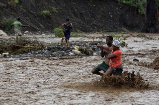 People cross an overflowing river using a rope and porters after a bridge washed away due to the pounding from Hurricane Matthew, which passed over Haiti on Oct. 4, 2016.