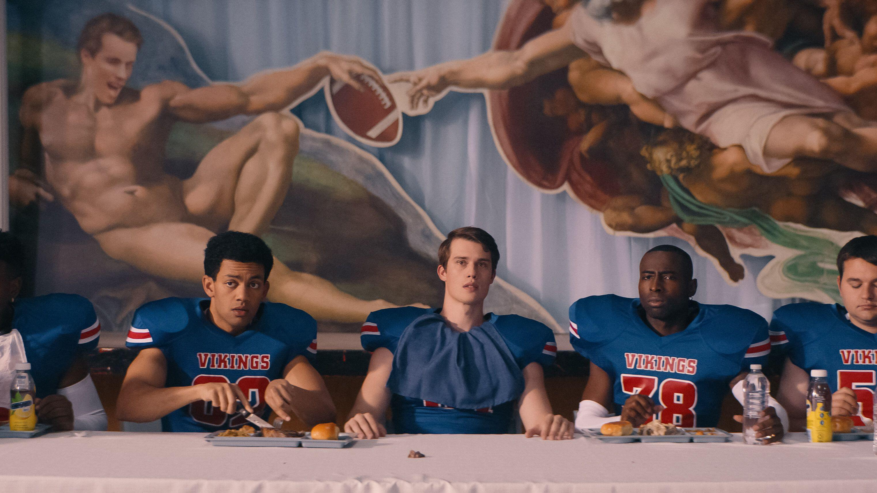 Jeff (Nicholas Galitzine, center) sits surrounded by his teammates in the cafeteria in a scene from "Bottoms" (2023)