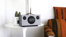 Audio Pro Addon T3+ in black and grey, sitting on white side table beside burnt orange sofa