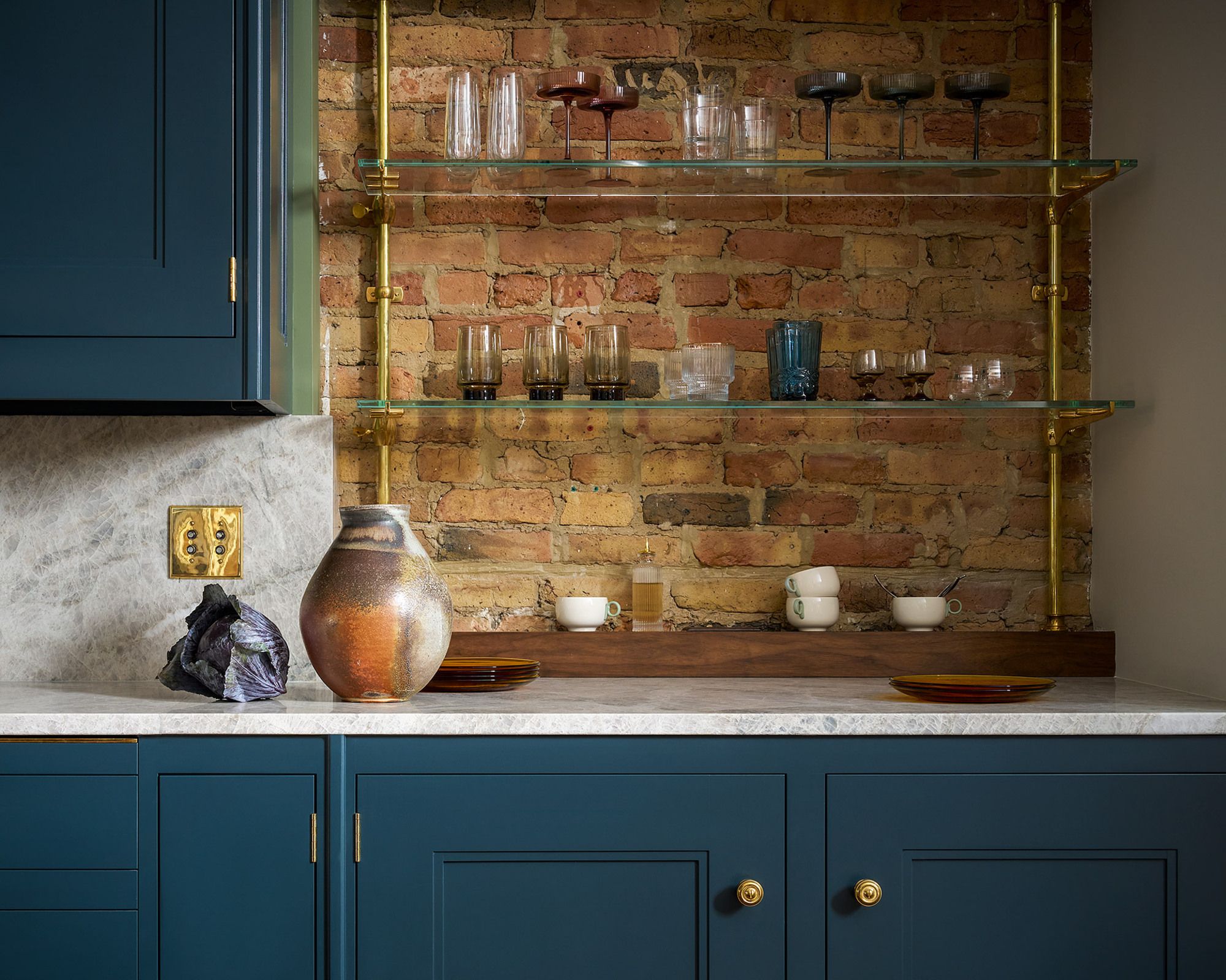 Dark teal blue cabinets with a bare brick wall behind. The backsplash and counter are a white marble 
