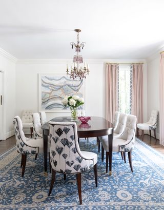dining room with blue patterned rug and dark wood table upholstered chairs with blue and white pattern ornate chandelier and pink curtains with patterned edge